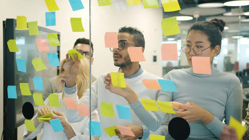 Diverse group of small business owners working at laptops and whiteboards, with charts showing revenue growth and savings metrics
